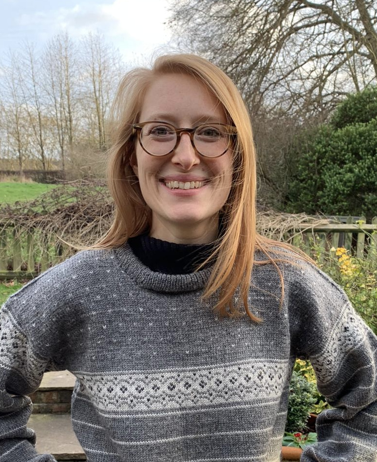 Image of women with shoulder length red hair, glasses, wearing a grey sweater