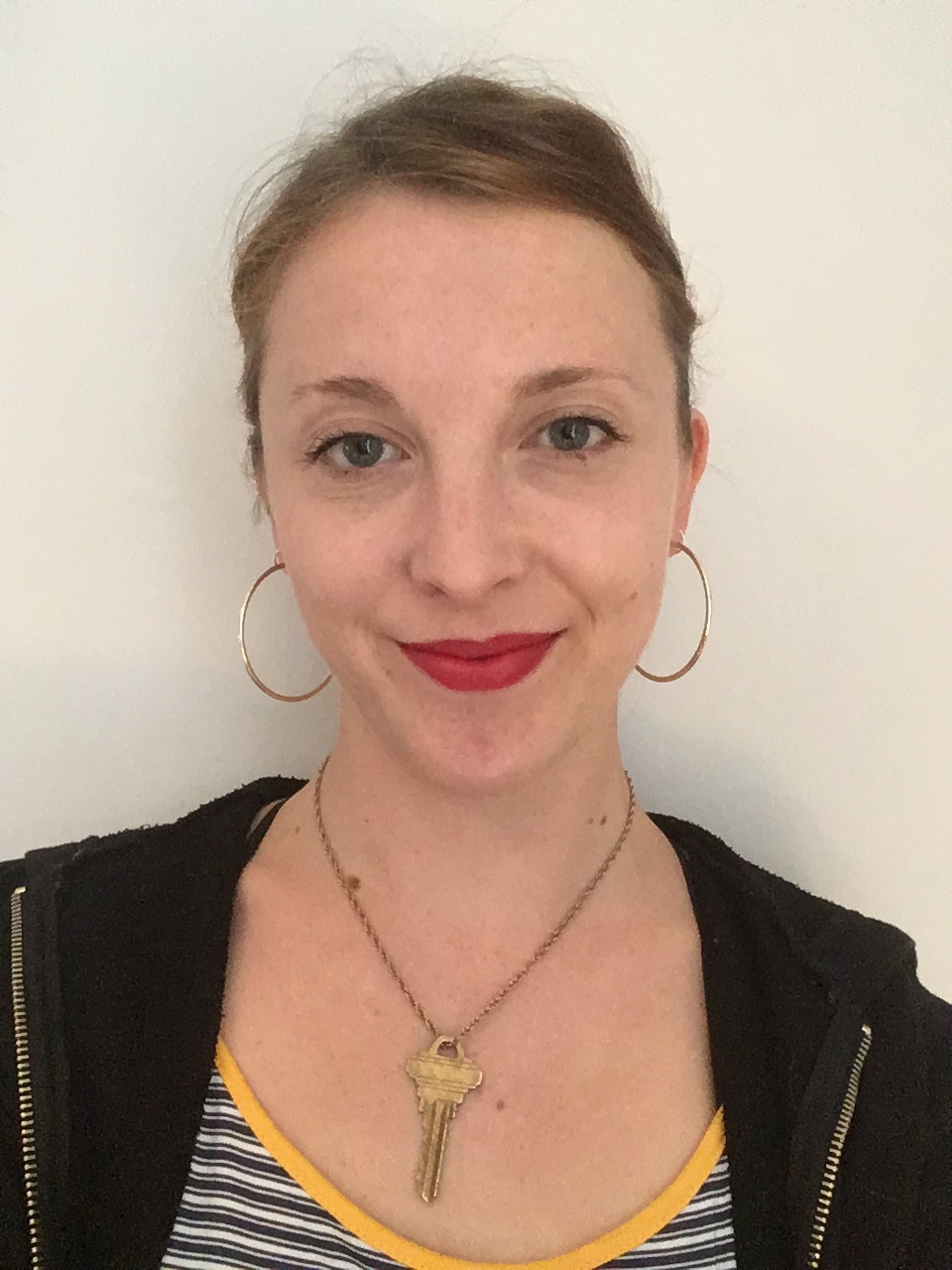 Photo of a white woman with hair pulled back. She is wearing red lipstick and a necklace. 