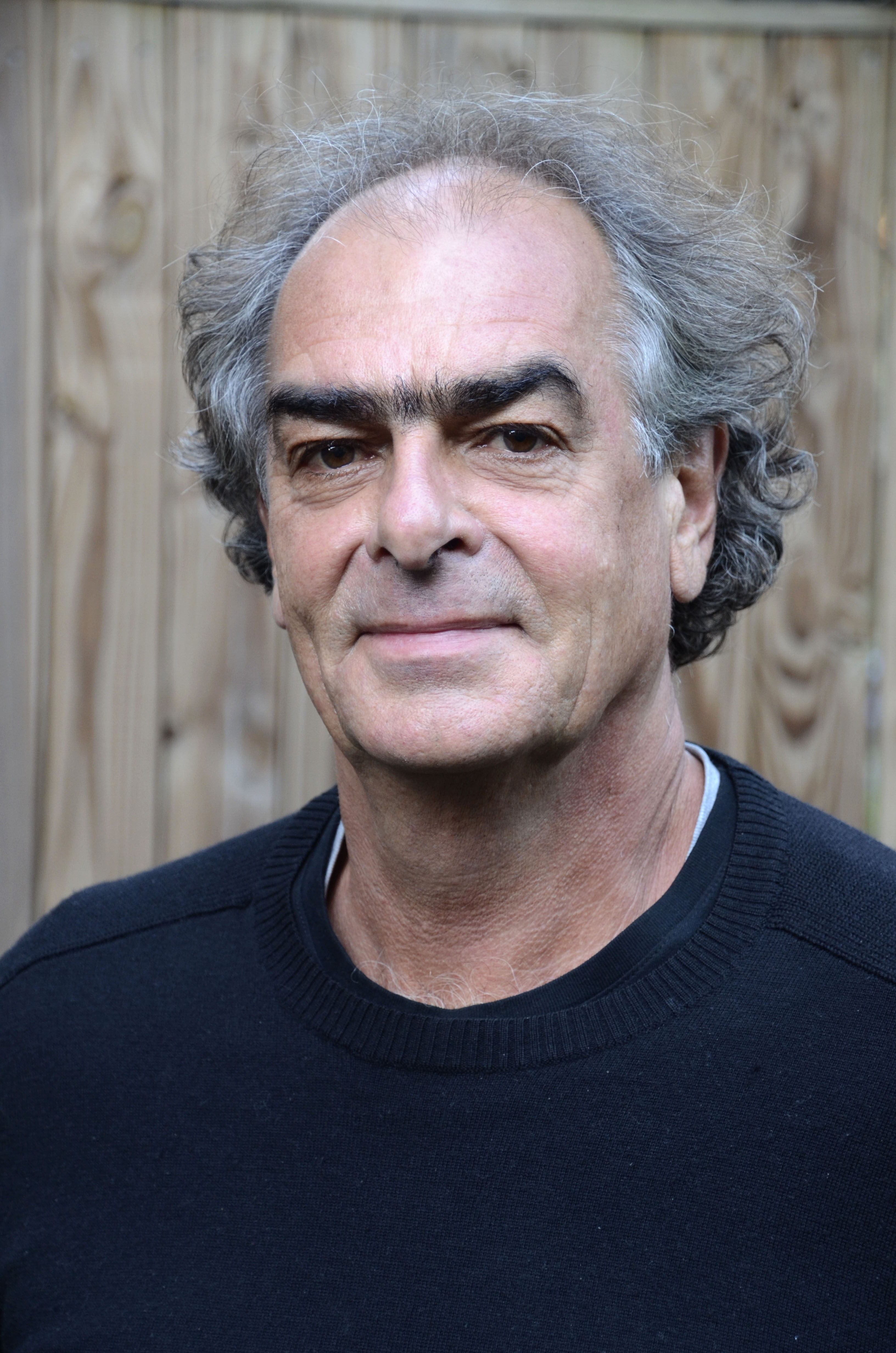 Man with grey hair and dark tshirt smiling at camera