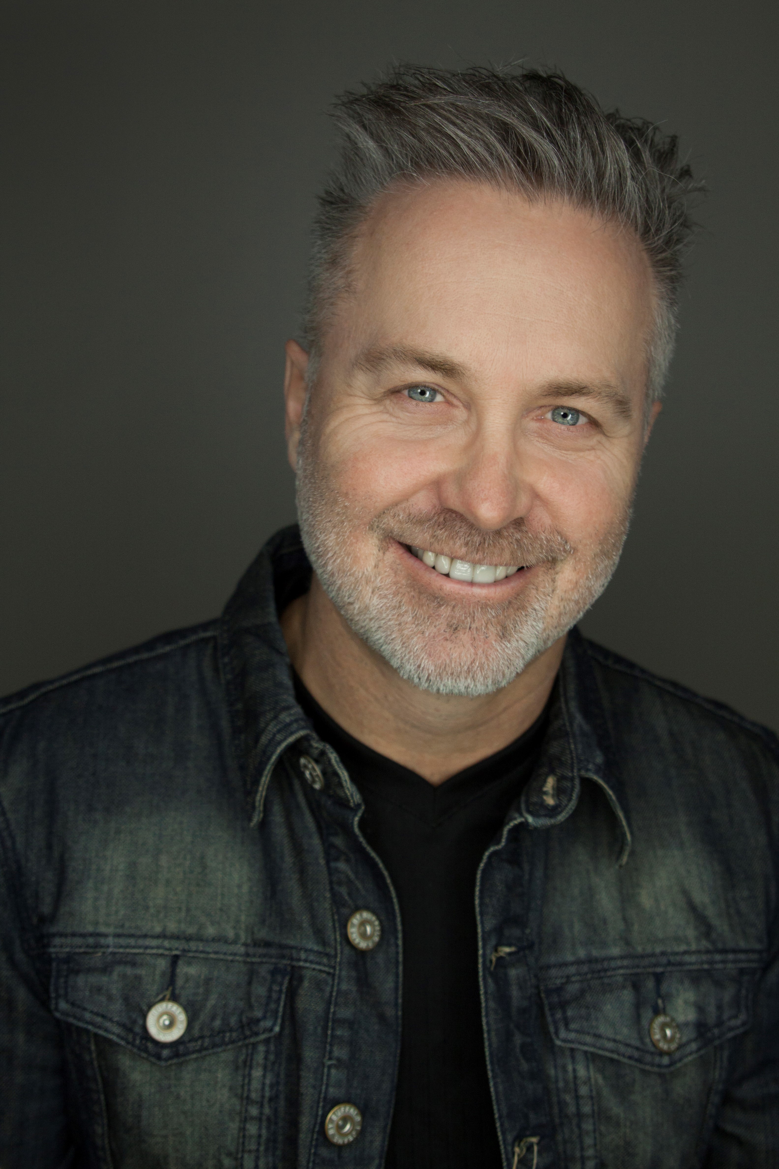 Photo of white man smiling at camera with grayish beard and plaid shirt 