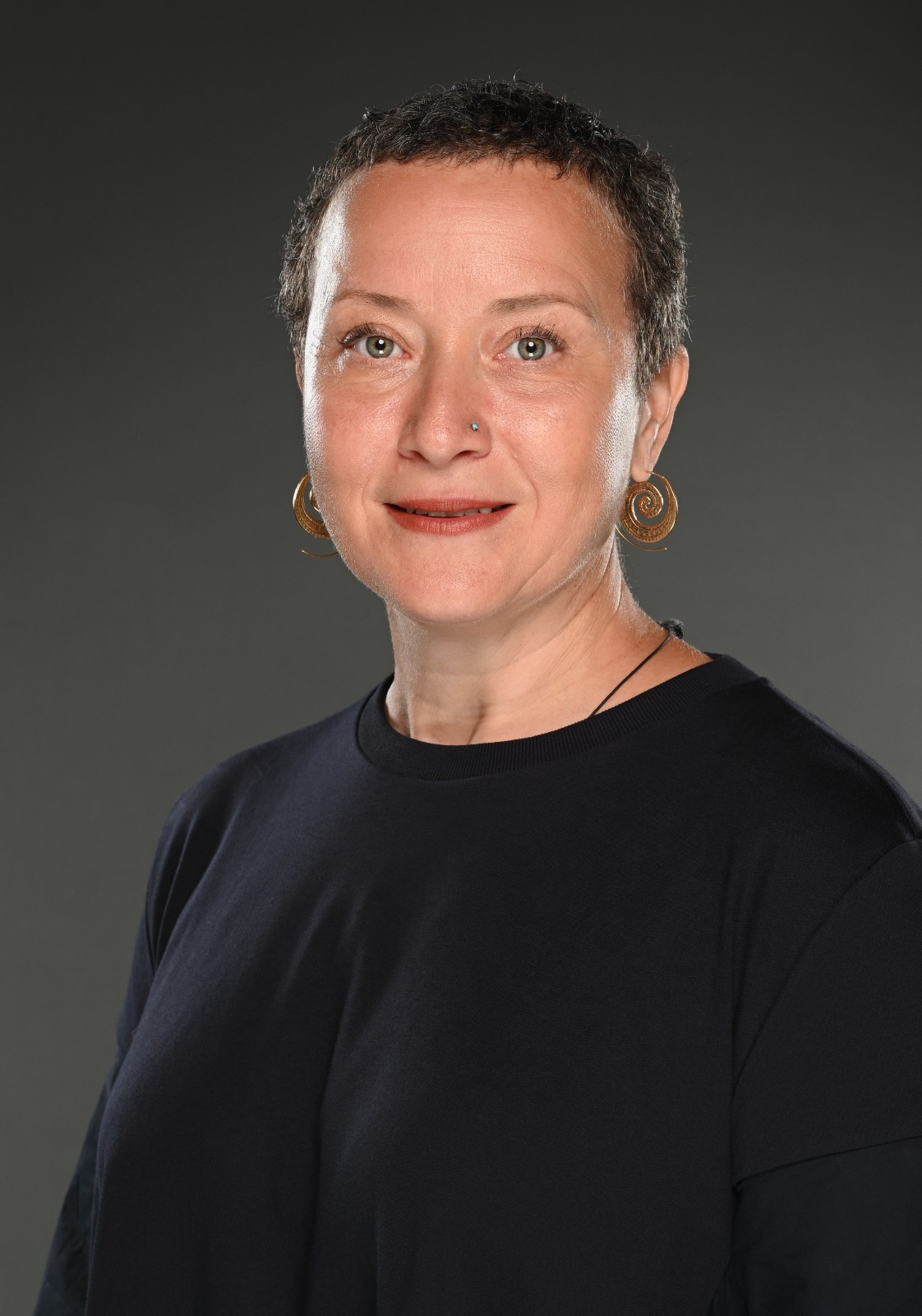 Woman with hair tied back wearing a black top looks at the camera