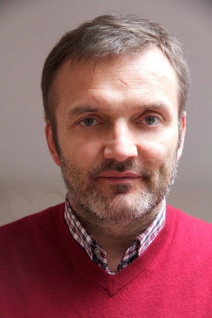 Man looking directly at camera wearing red sweater with grey hair and facial hair