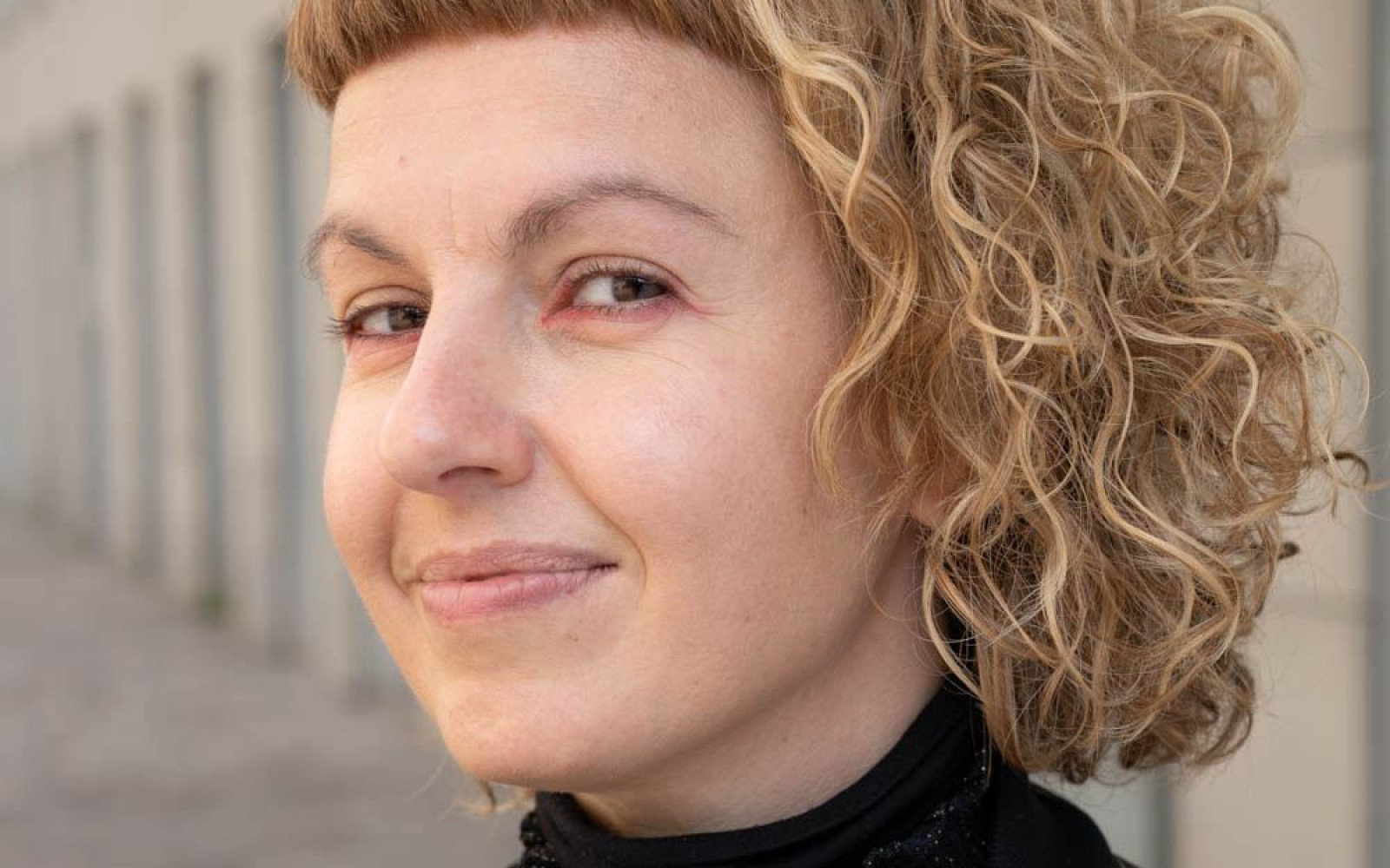 Close up of woman with curly blonde hair looking at camera smiling