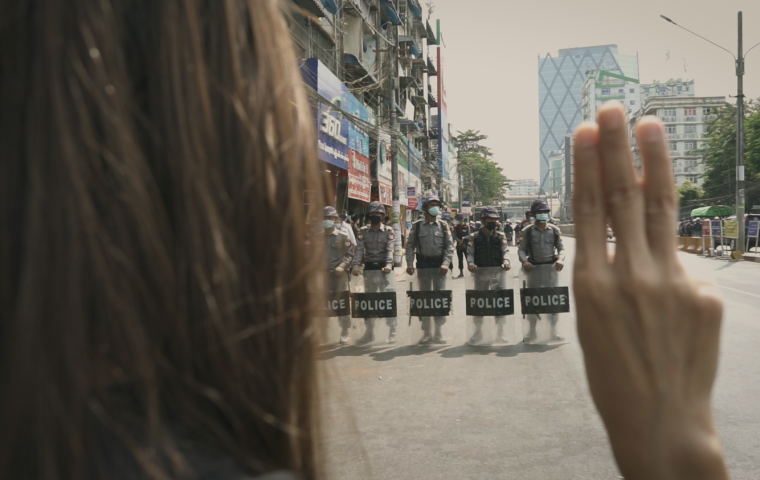 Woman standing in front of police holding three fingers up in protest