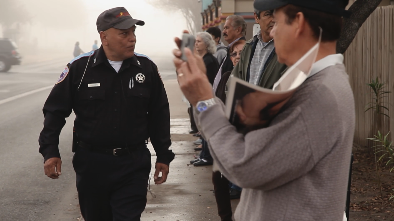 Photo of Latino man, a security guard looking at a crowd of anti-Abortion activists. 