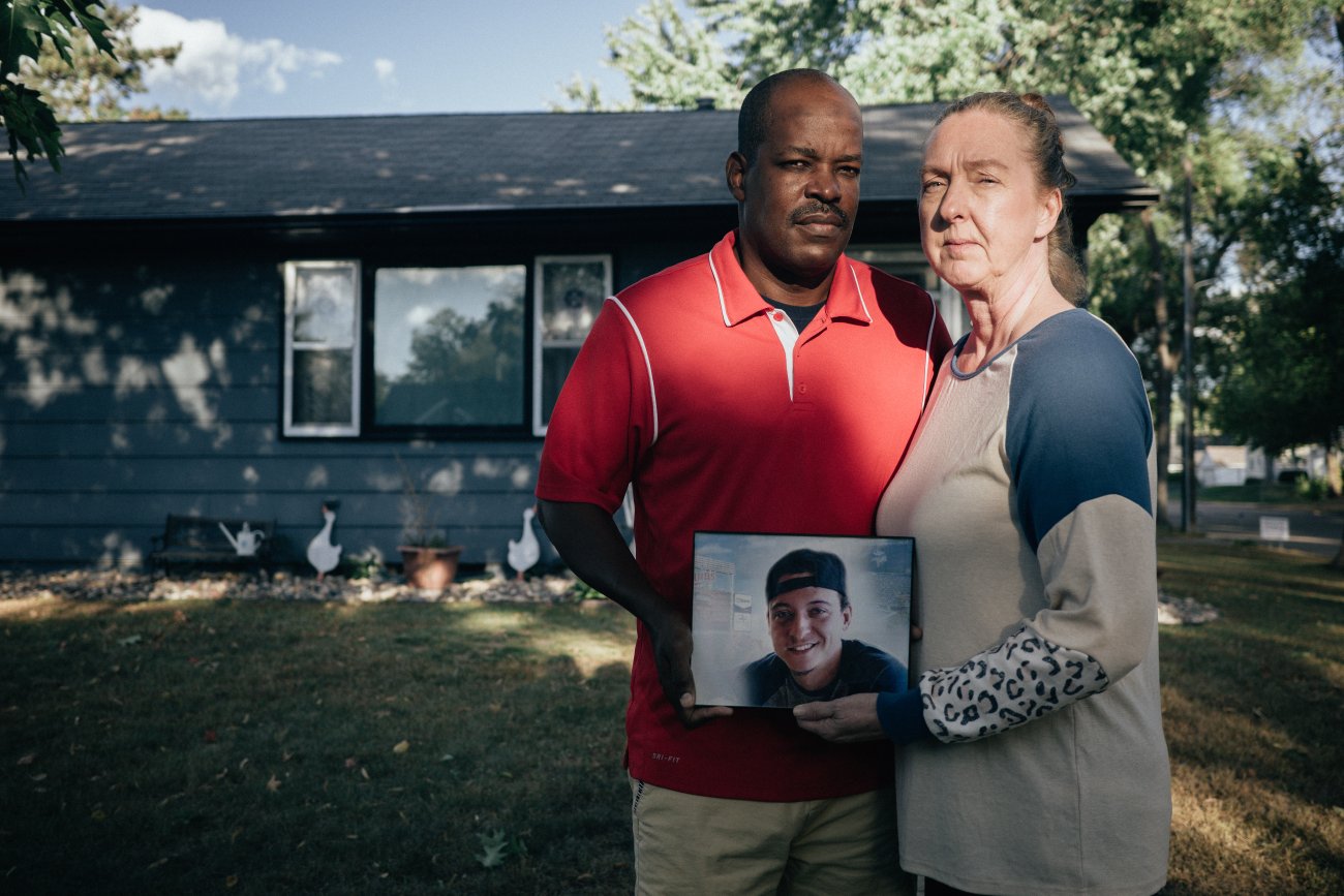 Photo of two parents, standing outdoors holding a photo of their son, who died due to rationing of insulin.