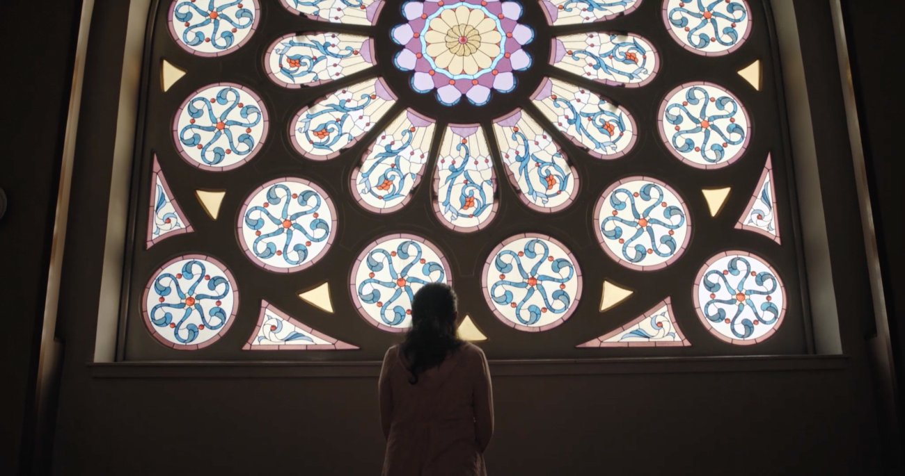 Image of a profile of a woman, facing a stained glass window 