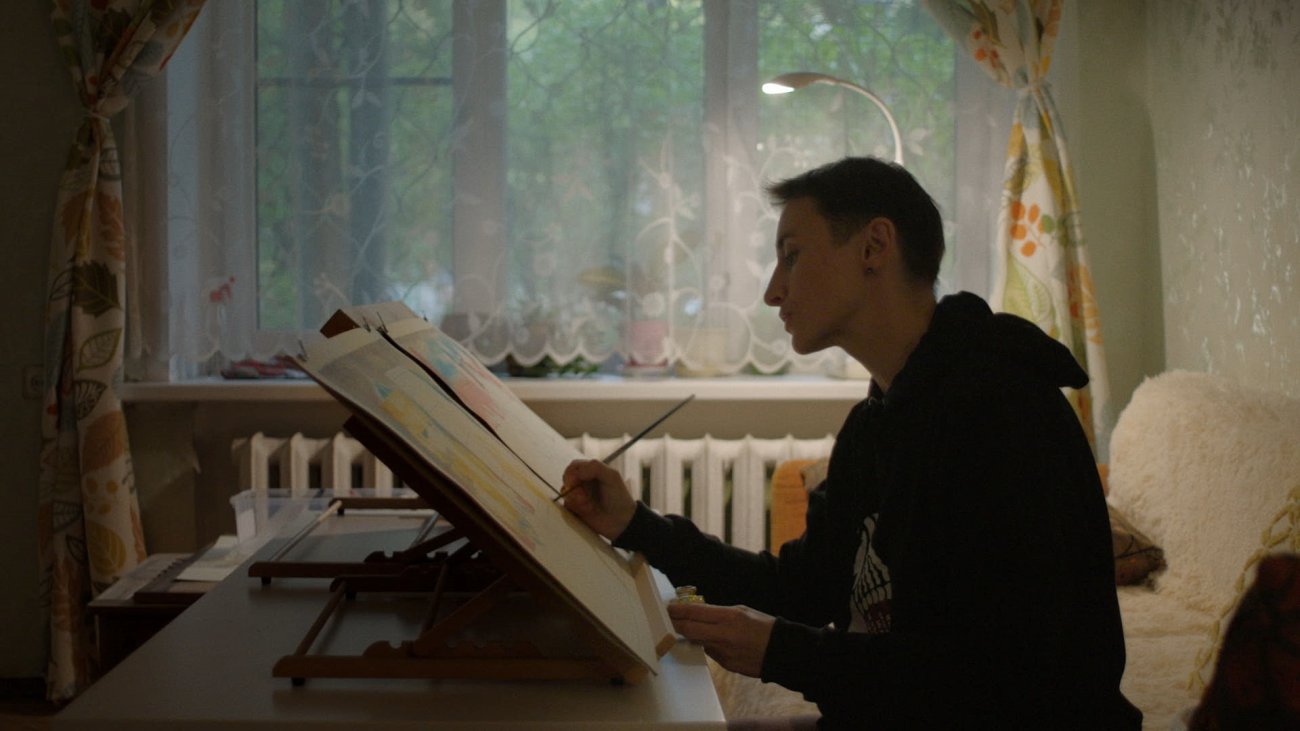 side portrait of a woman drawing at home at night with a window behind her