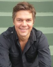 Headshot of man with short brown hair smiling at camera, wearing black shirt